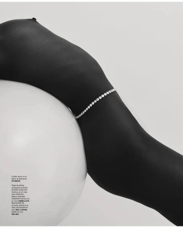 Woman's dark skin is adorned with a diamond bracelet, contrasting against a white spherical prop and clean background.