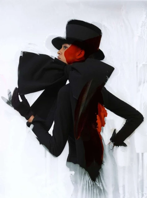 Fashion shot of an adult woman wearing a large black bow and hat, with artistic red and white wash effect on a white backdrop.