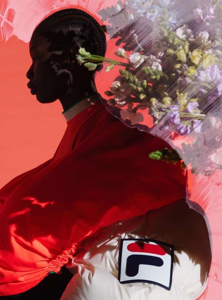 Profile shot of an African female model with braided hair adorned with flowers, wearing red top with the Fila logo visible on a white jacket.