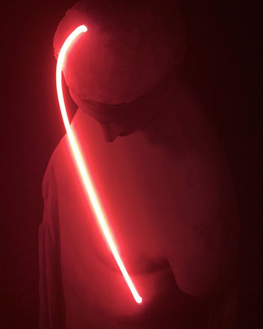 Monochromatic low-angle studio portrait of a light painting near the side of a mannequin's head in a dark shadowy setting.