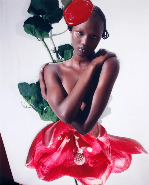 Striking fashion portrait of a Black woman with a red headpiece and flower dress, posing in a photo studio against a bright white background.