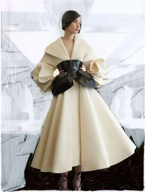 Fashion shot of a woman in a cream-colored dress with a black corset, posing against an abstract white and black painted backdrop.