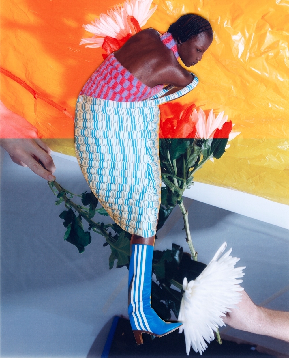Fashion editorial shot of a woman posing with white flowers, wearing a colorful top and striped skirt with matching blue boots.
