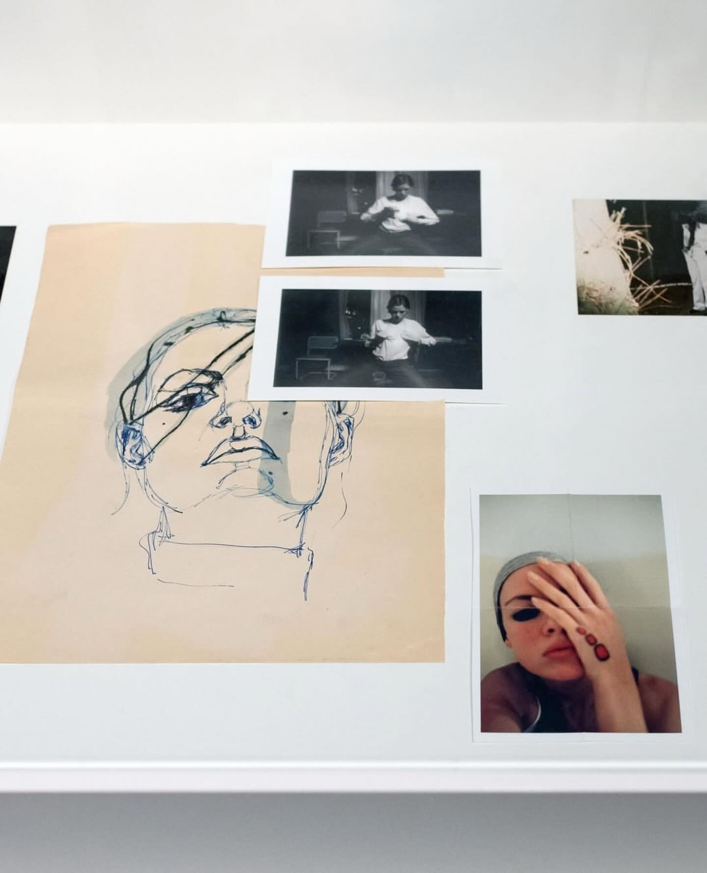 Art installation featuring a sketch of a woman's face, black and white photographs, and a color portrait on a white wall.