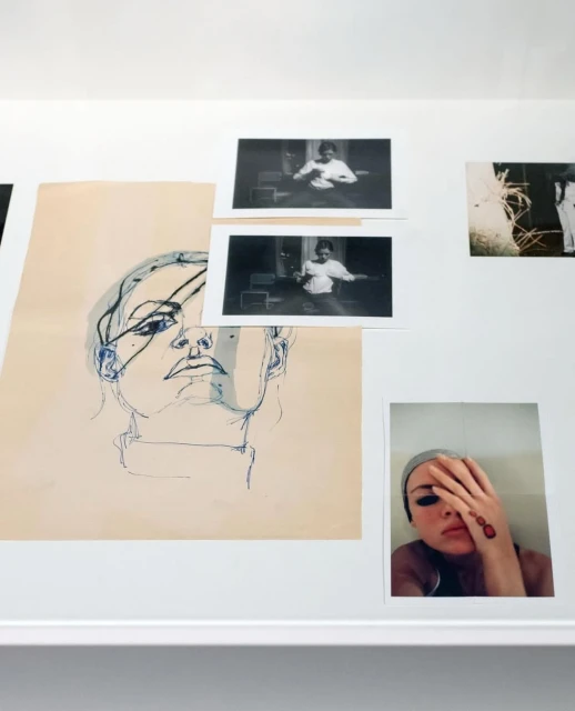 Art installation featuring a sketch of a woman's face, black and white photographs, and a color portrait on a white wall.