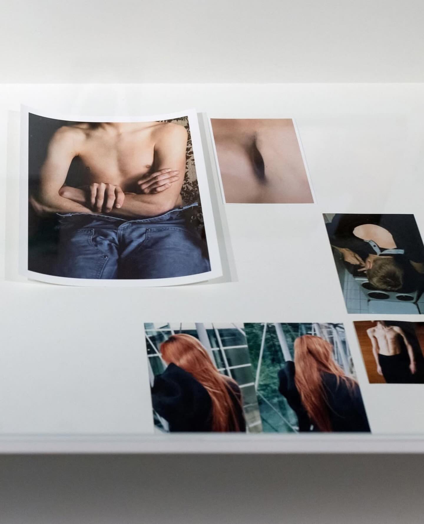 Display of art photographs on a white surface featuring male and female torsos, and portrait shots with red hair.