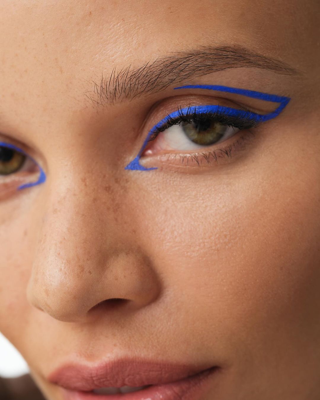 Close-up of a woman's face with bold blue graphic eyeliner. Beauty shot emphasizing graphic makeup, cosmetic artistry, and vibrant color.