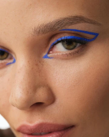 Close-up of a woman's face with bold blue graphic eyeliner. Beauty shot emphasizing graphic makeup, cosmetic artistry, and vibrant color.