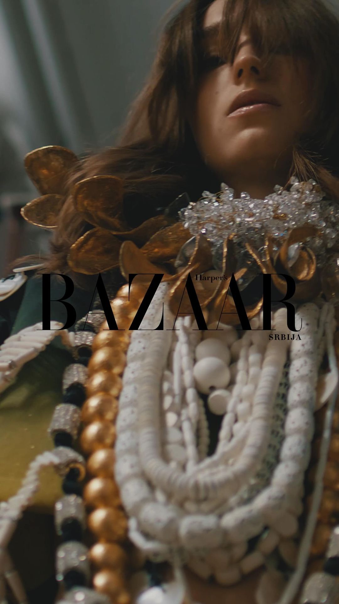 Fashion editorial shot of a woman wearing ornate jewelry and a golden, jeweled top against a blurred background with text overlay.
