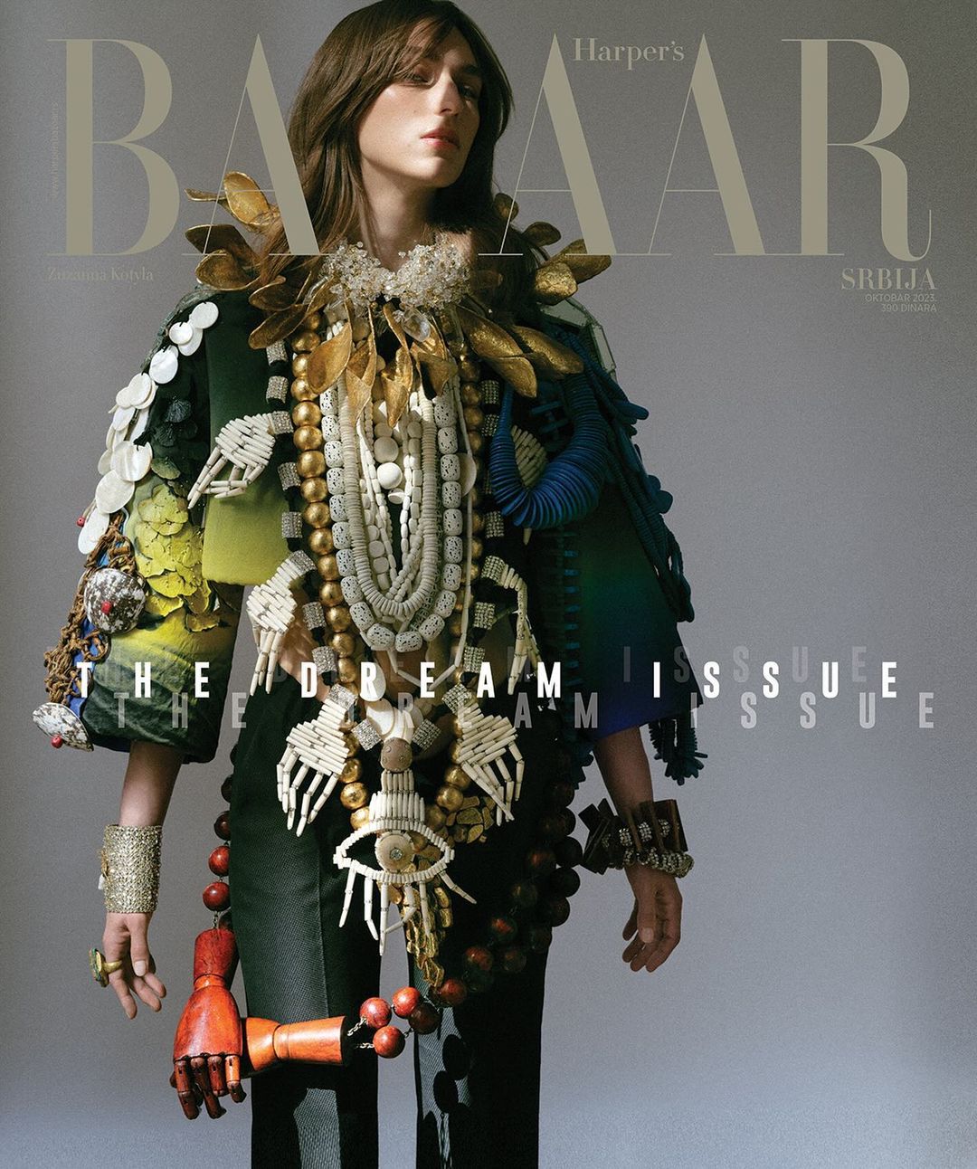 Magazine cover featuring a fashion model in an elaborately decorated green jacket, adorned with necklaces, beads, and a wooden hand.
