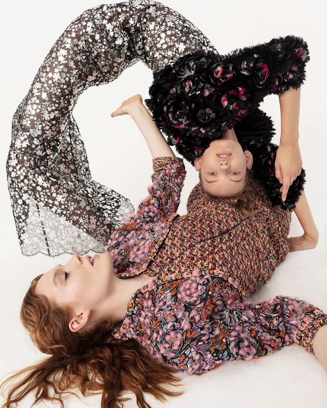 Two models pose creatively in a studio setting, wearing floral-patterned outfits. One model is upside down with a black floral top.