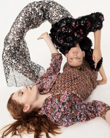 Two female models in patterned garments posed in an arched, interlocking posture against a plain white background.