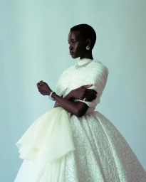 Model with short hair wearing a white textured ballgown and silver jewellery against a pale blue background.