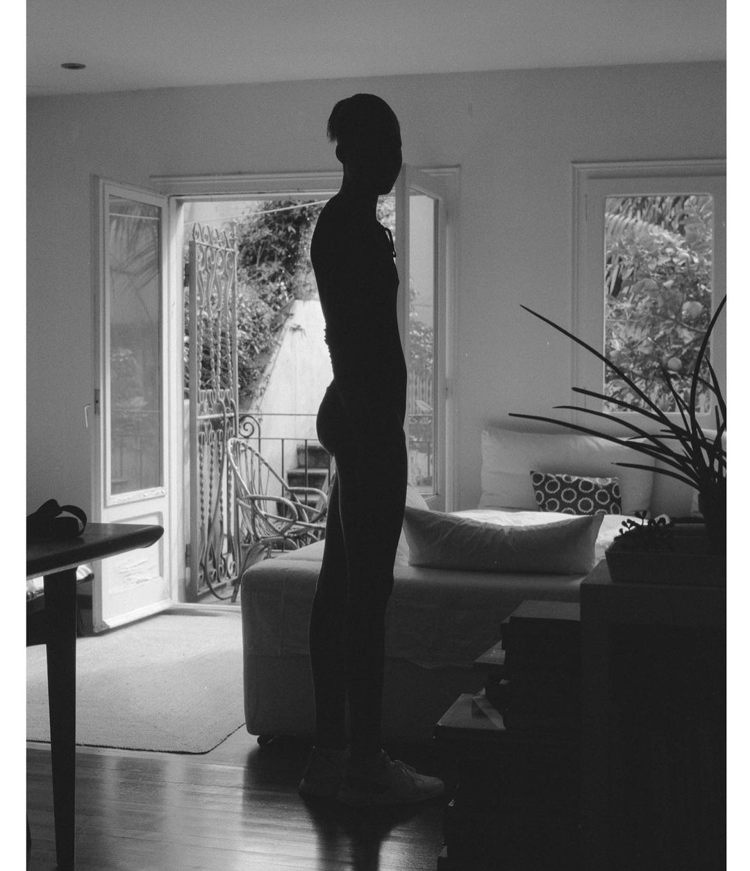 Silhouette of a person standing indoors against an open doorway leading to a balcony.