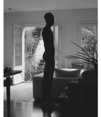 Silhouette of a person standing indoors against an open doorway leading to a balcony.