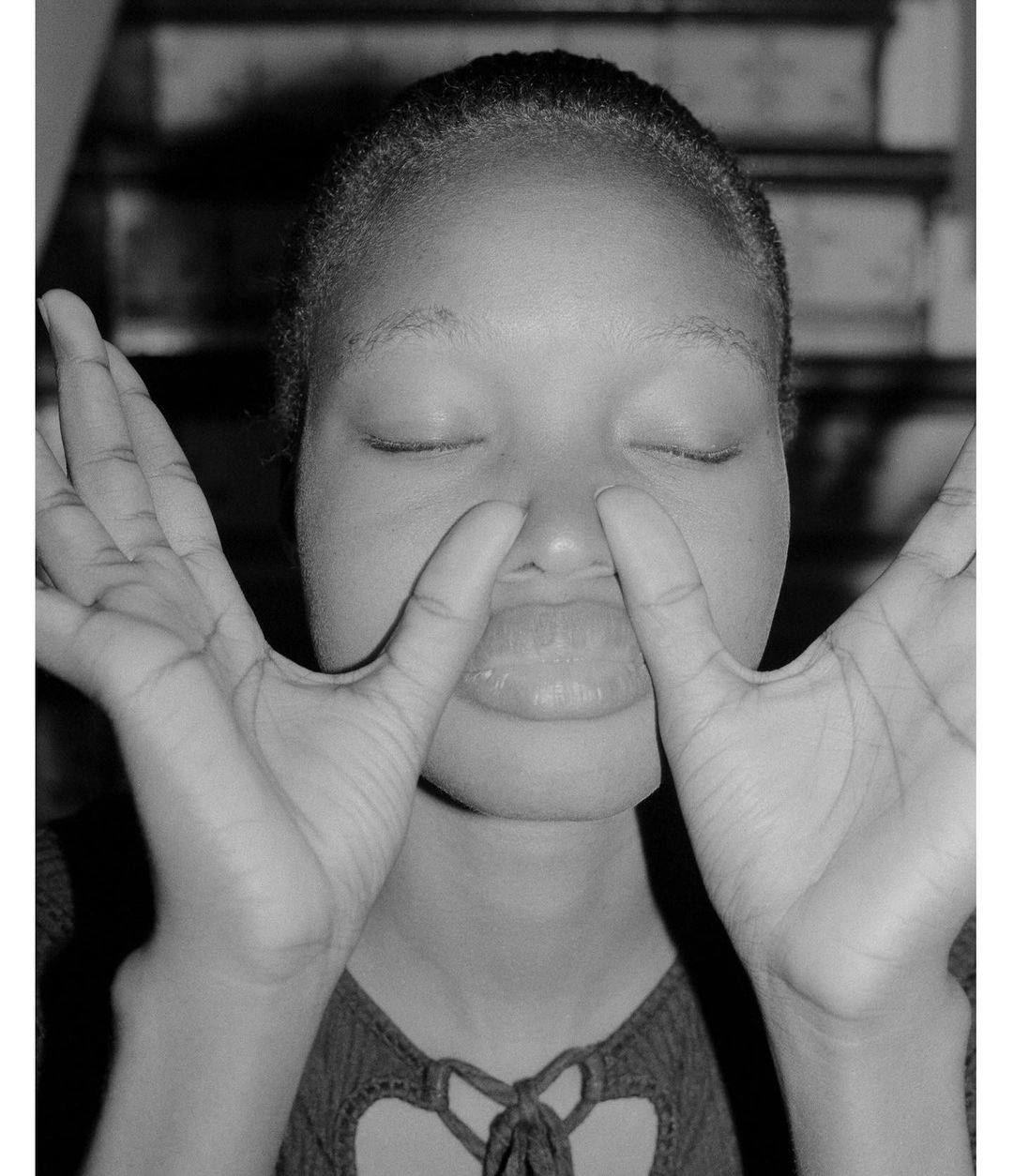 Portrait of an adult Black woman with closed eyes, framing her face with her hands in front of a background of white stairs.