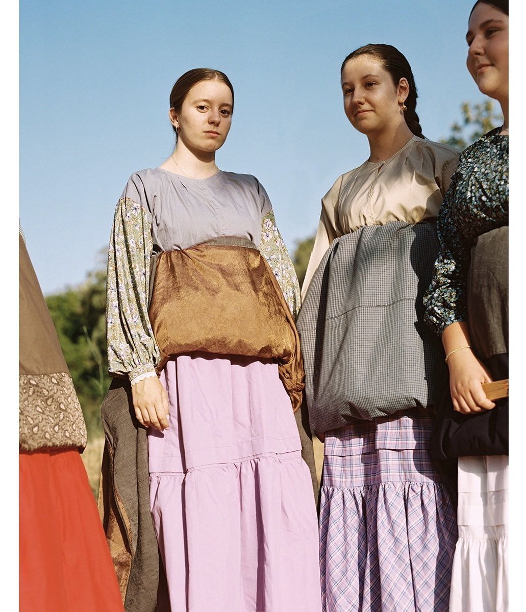 Three young women in vintage-style dresses pose outdoors against a clear blue sky, showcasing a blend of floral prints and solid fabrics.