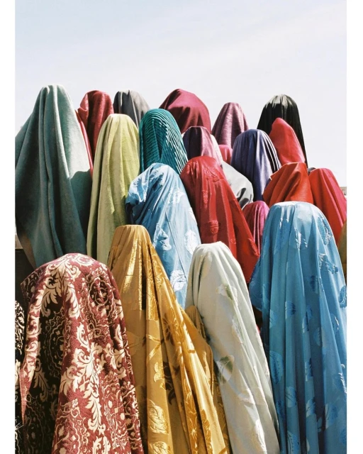 Many colorful rolls of fabric draped vertically in an arrangement, showcasing various patterns and textures under bright daylight.