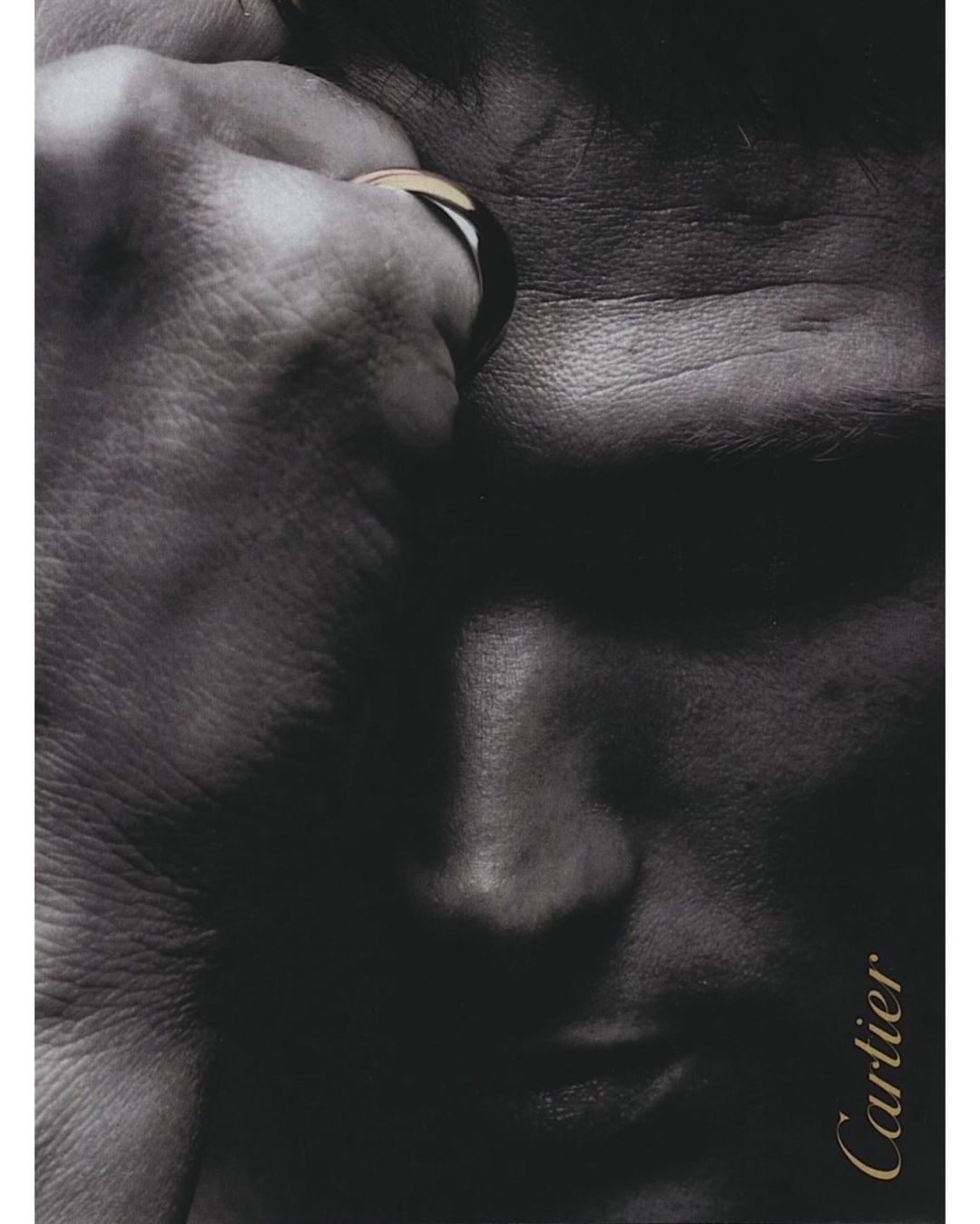 Monochromatic portrait of a male face with a gold ring on his finger, accented by the elegant Cartier logo in gold.