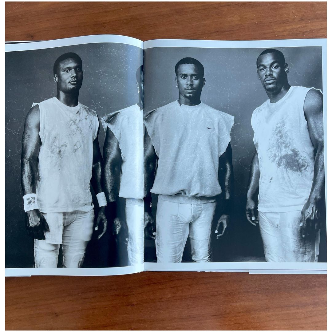 Three athletic adult males in sleeveless shirts pose in a black and white portrait featured in an open magazine on a brown surface.