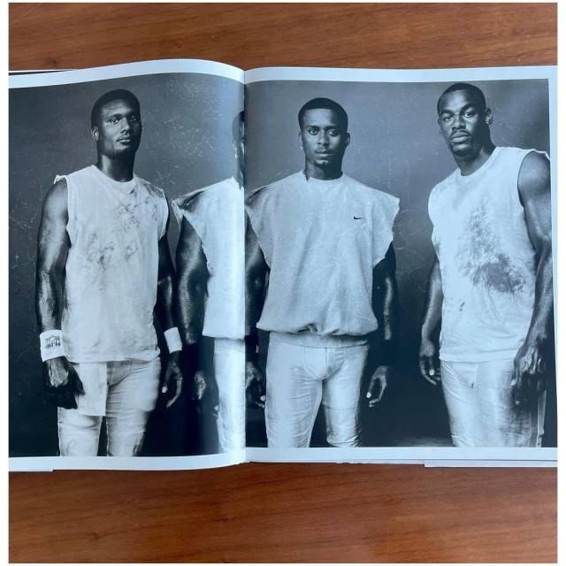 Three athletic adult males in sleeveless shirts pose in a black and white portrait featured in an open magazine on a brown surface.