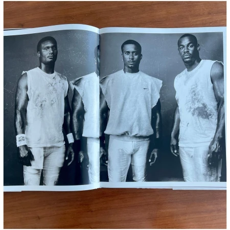Three athletic adult males in sleeveless shirts pose in a black and white portrait featured in an open magazine on a brown surface.