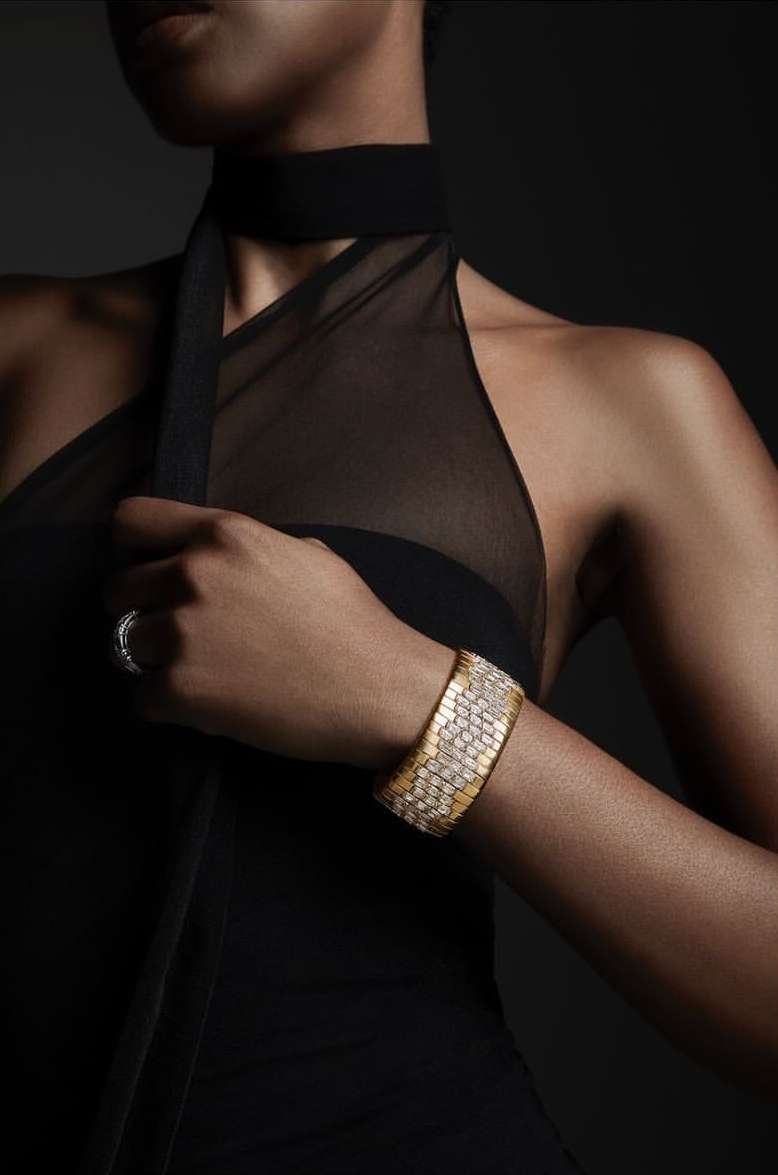 Woman wearing a gold and diamond cuff bracelet with a diamond ring, in a black dress against a dark background.