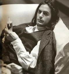 Portrait of Marc Jacobs with long dark hair holding a cigarette, wearing a tweed vest and white shirt, photographed by Walter Chin.