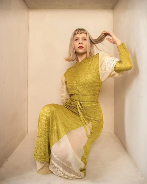 Elegant woman in an olive green dress, posing in a studio, with light blonde hair and a unique outfit, captured in a vertical composition.