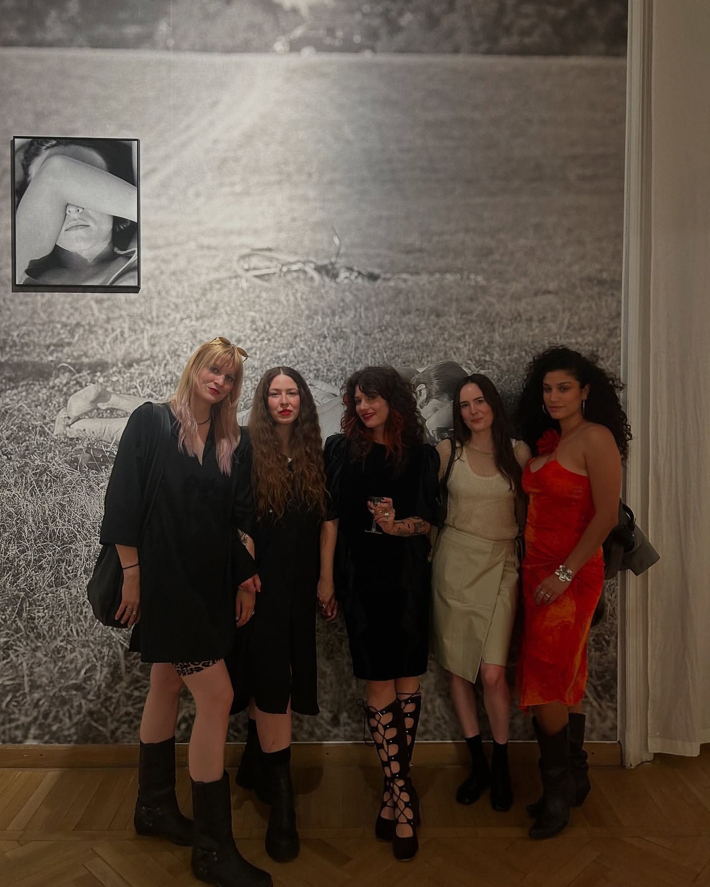 Five women posing together in front of a large black and white landscape photo wall by photographer Wanda Martin in London.