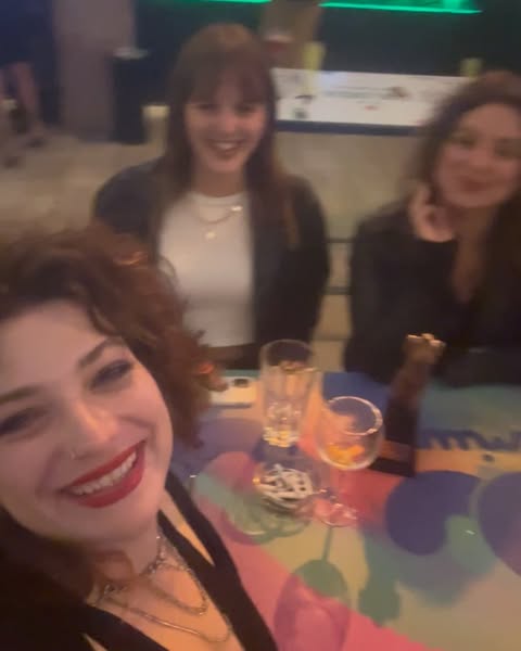 Three young women smiling together in a dimly lit bar interior by photographer Wanda Martin.