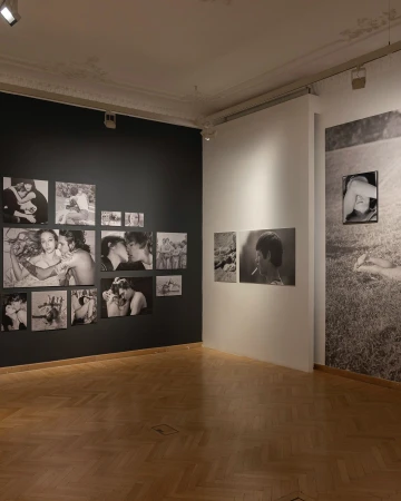 Art gallery interior featuring black and white photographs displayed on walls, with herringbone wood flooring.