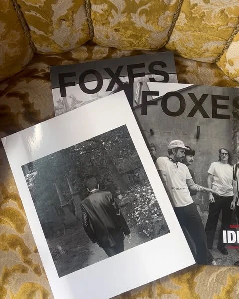 Close-up shot of three Foxes magazine covers stacked on a textured yellow patterned sofa. Black and white photography featured.