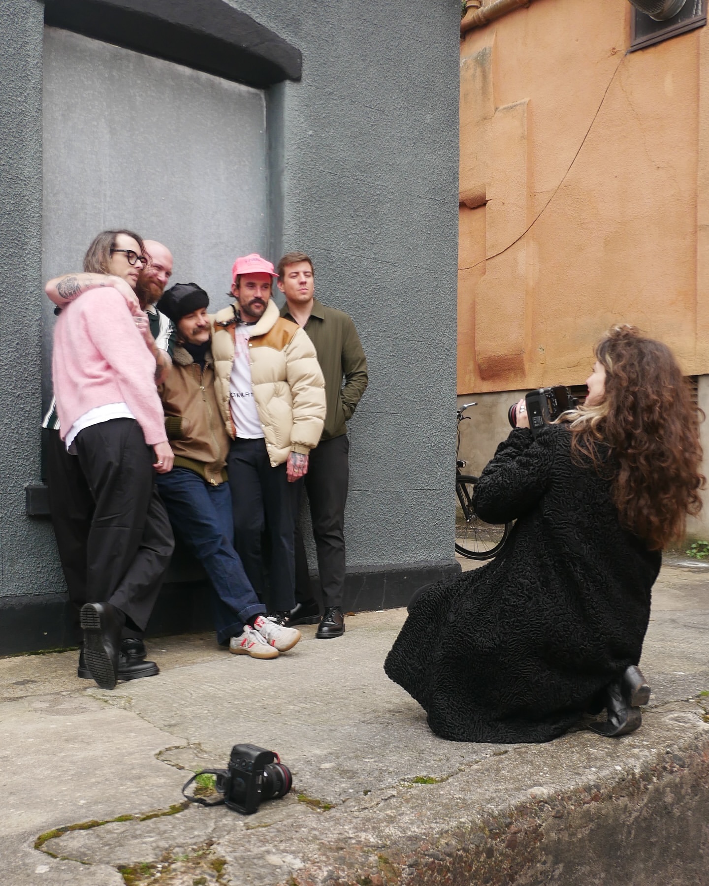 Group of five people posing for a photo outdoors on a city street with a photographer taking the picture. Buildings in the background.