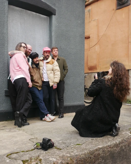 Group of five people posing for a photo outdoors on a city street with a photographer taking the picture. Buildings in the background.