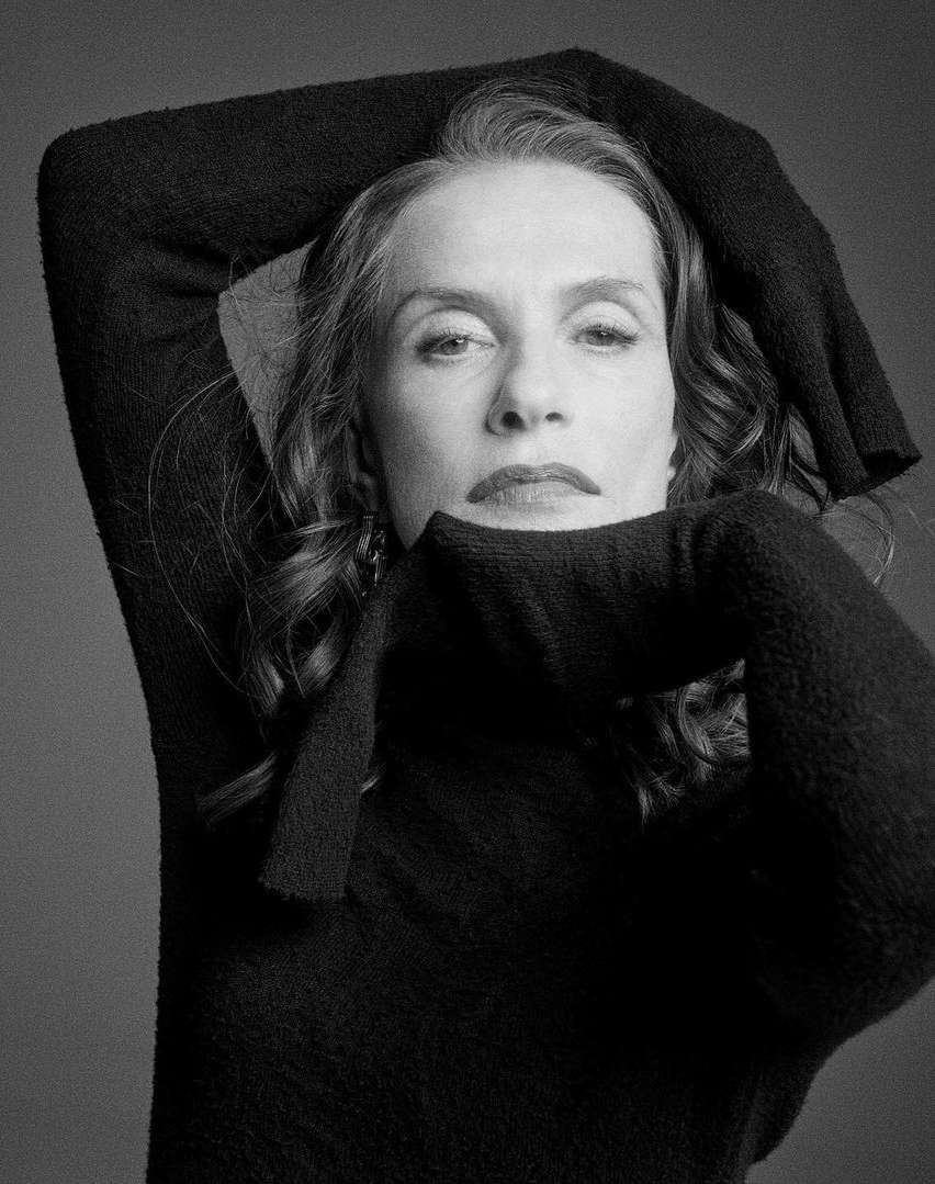 Black and white portrait of an adult woman with dark hair in a dark sweater. She is gazing at the camera with her arms above her head.