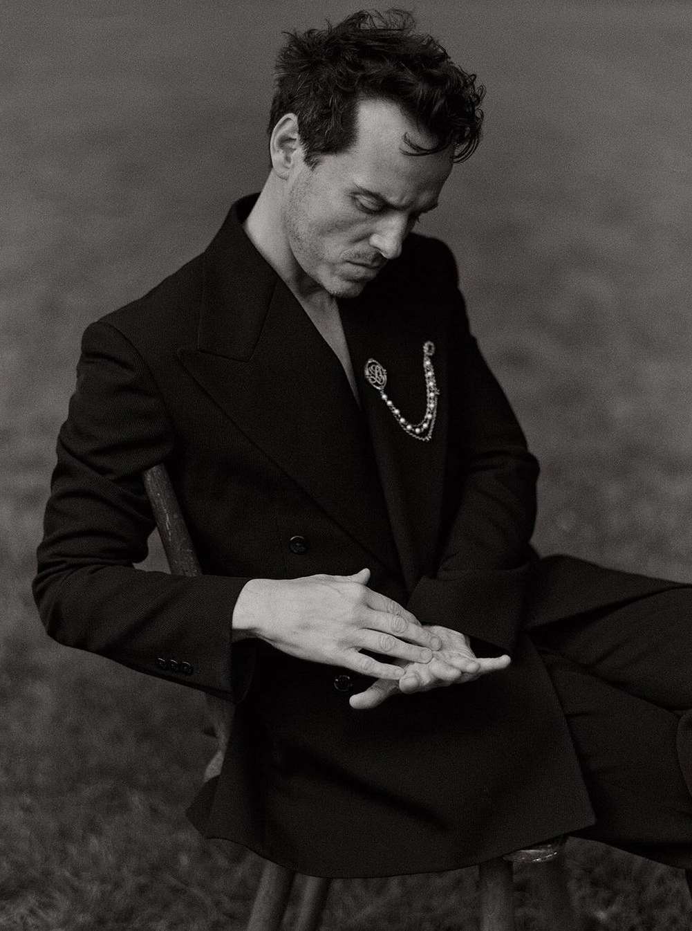Monochrome portrait of a man in a black suit seated in a grassy outdoor setting, showcasing a classic, elegant, and contemplative pose.