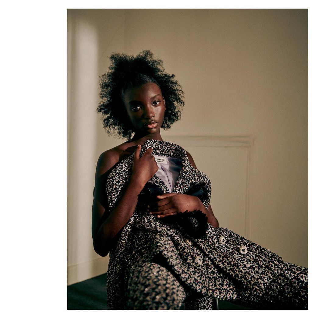 Portrait of a Black fashion model in black and white patterned couture outfit, posing indoors in soft lighting against a neutral wall.