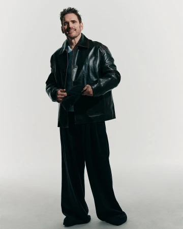 Matt Dillon wearing a dark leather jacket and wide trousers against a light grey background, photographed by Ward Ivan Rafik.