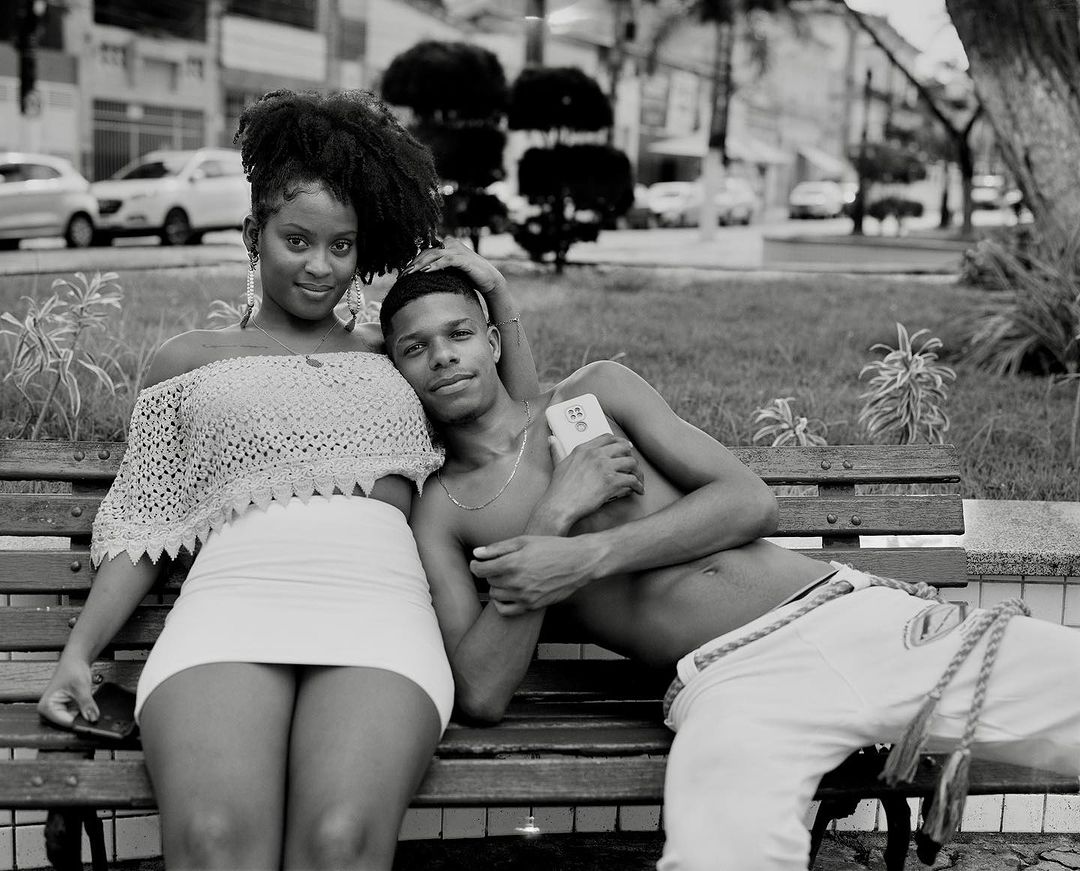 Monochrome portrait of a stylish young couple sitting on a park bench on an overcast day, sharing a moment with cell phones in hand.