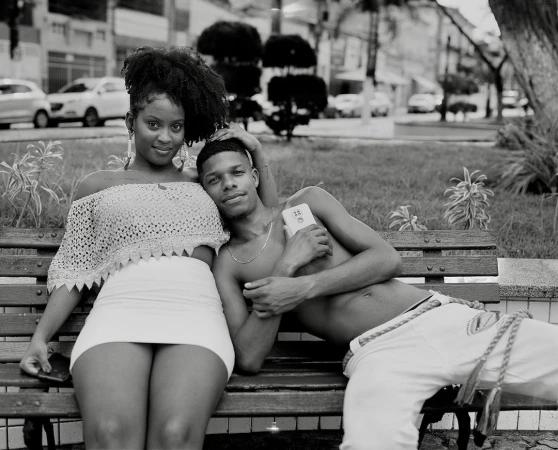 A black man and woman sitting together on a wooden park bench, captured in monochrome by Wayne Lawrence.