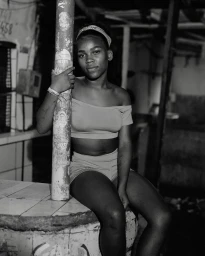 Black-and-white portrait of a young Black woman sitting on a counter holding a pole, photographed by Wayne Lawrence in New York.