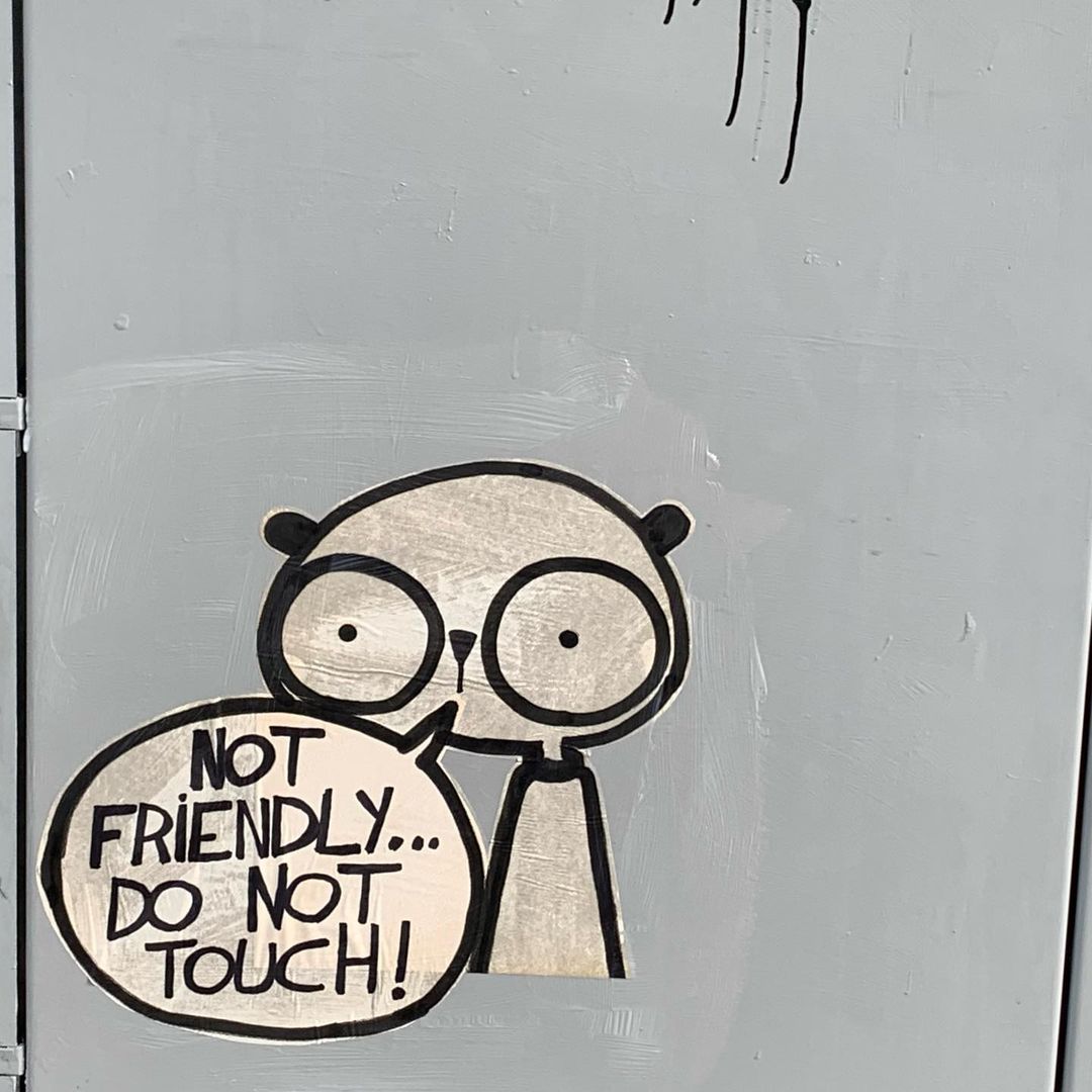 Cartoon character sticker on a gray surface with a speech bubble saying 'Not Friendly...Do Not Touch!' Dark cartoon illustration style.
