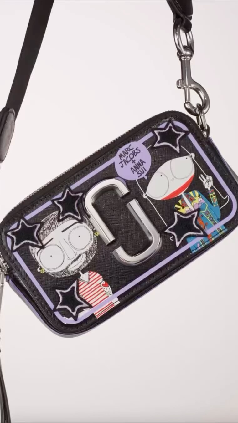 Close-up of a black Marc Jacobs purse with a silver logo, cartoon characters, and star details on a white background.