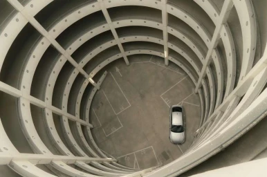 High-angle view down a multi-level circular parking garage with a single silver car parked at the bottom level.