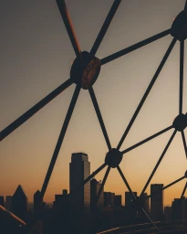 View of a city skyline at sunset through a geometric metal framework structure from a high vantage point