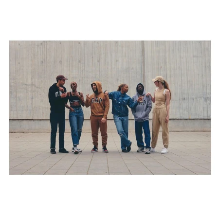Group of six diverse young adult models in casual clothing by GAP standing in front of a concrete wall, posing in an outdoor setting.