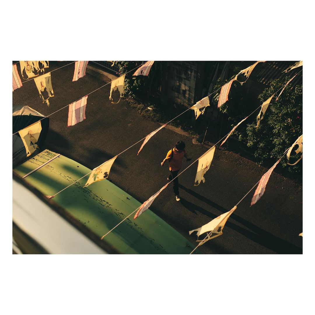 Overhead shot of an adult male walking on an asphalt road flanked by a green structure and strings of pennant flags.