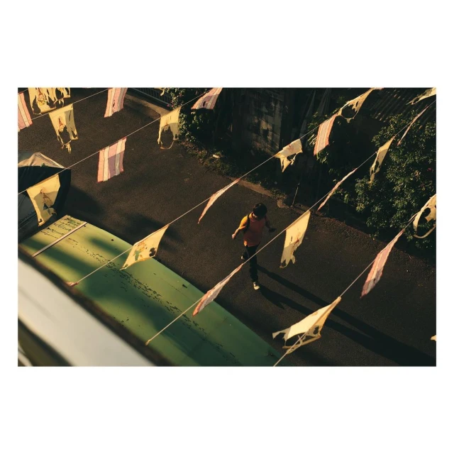 Overhead shot of an adult male walking on an asphalt road flanked by a green structure and strings of pennant flags.