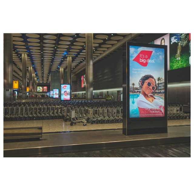 Airport terminal interior showcasing luggage carts and a Virgin Holidays advertisement featuring a woman in sunglasses by a pool.